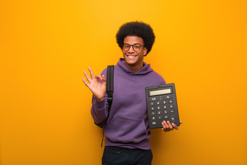 Young african american student man holding a calculator cheerful and confident doing ok gesture
