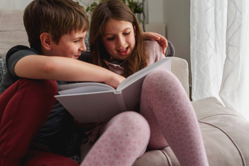 Boy and a girl reading a book, smiling at home. Brother and sister. First love