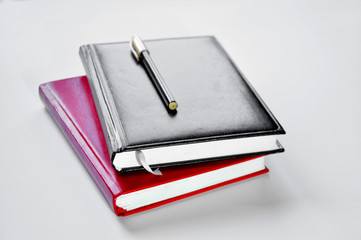two notebooks and pen are on the table on a white background