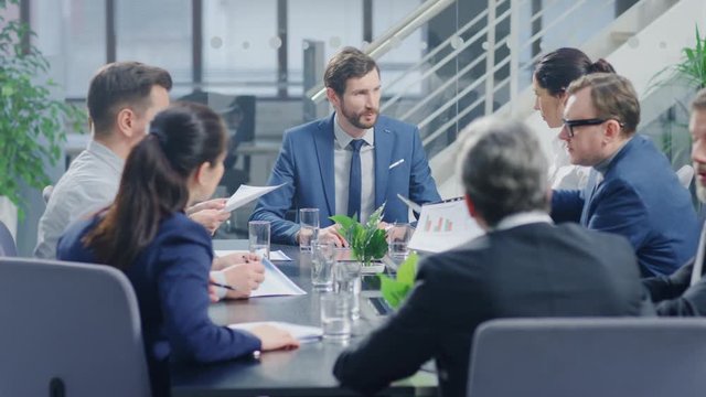 In the Modern Corporate Office Meeting Room: Diverse Group of Businesspeople, Lawyers, Executives and Members of the Board of Directors Talking, Negotiating, Use Documents and Consult Statistic Graphs
