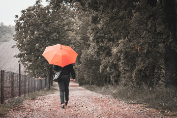 woman with orange umbrella walking gravel road
