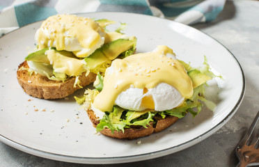 Eggs Benedict with avocado on concrete background.