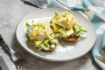 Eggs Benedict with avocado on concrete background.