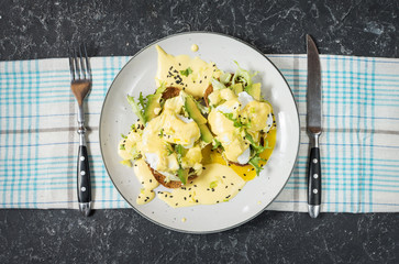 Eggs Benedict with salad and avocado on stone background.