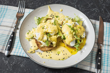 Eggs Benedict with salad and avocado on stone background.