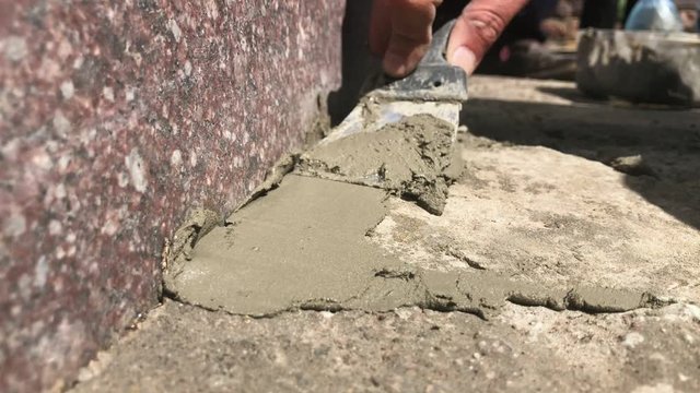 Hand with putty knife repair cracks with cement in the floor at the cemetery. Slow motion