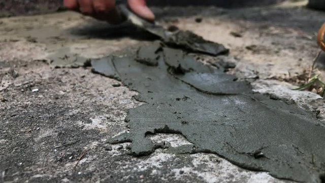 Hand with putty knife repair cracks with cement in the floor at the cemetery. Slow motion
