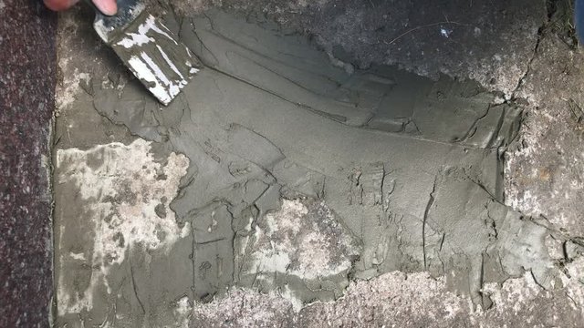 Hand with putty knife repair cracks with cement in the floor at the cemetery. Slow motion