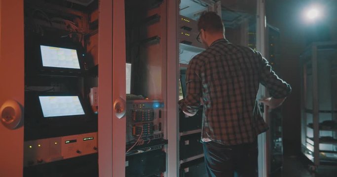 Young male programmer in eyeglasses connects wire to computer