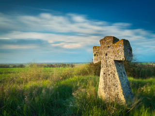 stone cross on old cemetery with sunset sun and blurred clouds