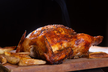 Delicious roasted chicken with potatos in a wooden table with black background