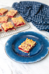 Freshly Baked Strawberry Bar Cookies cooling on a wire rack, one isolated in front on blue plate, blue kitchen towel, white countertop