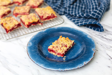 Freshly Baked Strawberry Bar Cookies cooling on a wire rack, one isolated in front on blue plate, blue kitchen towel, white countertop