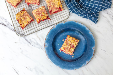 Freshly Baked Strawberry Bar Cookies cooling on a wire rack, one isolated in front on blue plate, blue kitchen towel, white countertop