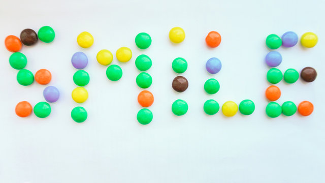 Phrase SMILE made of color candies on white background