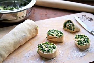 Cooking homemade buns with green onions, nettles, cheese and egg, the second step. Folding the roll with the filling and cutting it into buns. Selective focus. Wild herbs cooking.