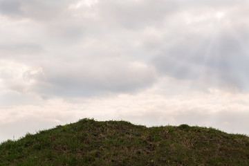 A hill with grass against a cloudy sky