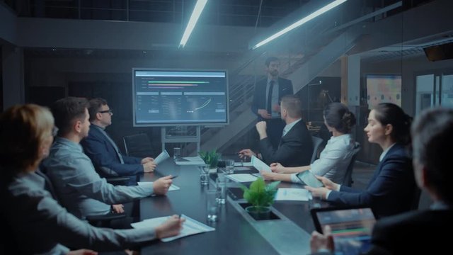 In the Corporate Meeting Room: Male Executive Talks and Uses Digital Interactive Whiteboard for Presentation to a Board of Directors, Investors. Screen Shows Growth Data. Late at Night Office