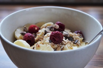 cereals in a bowl with bananas and raspberries