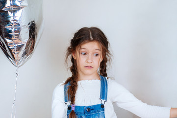 Happy beautiful little girl holding a silver gel balloon in the form of numbers. Birthday celebration.