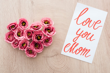 top view of heart sign made of eustoma flowers and card with love you mom lettering on wooden table