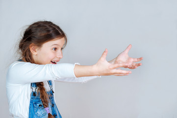 Adorable girl pointing at empty space, emotional portrait. Smiling kid in denim overalls presenting sale discount