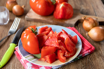 Whole and sliced tomatoes on cutting board and ceramic plate and whole onion in the background. Old wooden table.