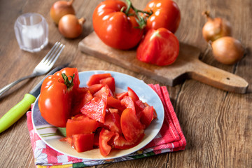 Whole and sliced tomatoes on cutting board and ceramic plate and whole onion in the background. Old wooden table.
