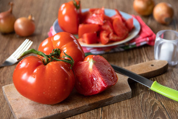 Whole and sliced tomatoes on cutting board and ceramic plate and whole onion in the background. Old wooden table.