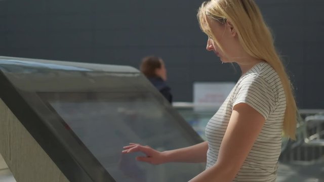 Woman using interactive touchscreen display at mall - scrolling and touching.