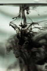 a cloud of ink in a transparent glass cup with clear water against the backdrop of a striped screen with rays of light. Template, layout, background, texture. macro diffusion black and white
