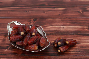Islamic festival of Ramadan concept. Delicious tropical dates on a silver plate on a brown pine wooden table background. Traditional Middle East culture. Ramadan Kareem