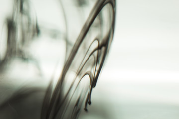 a cloud of ink in a transparent glass cup with clear water amid rays of light. Template, layout, background, texture. macro diffusion black and white abstraction