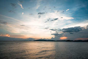 sunset cloudy  sky, clean water, small hills on the horizon