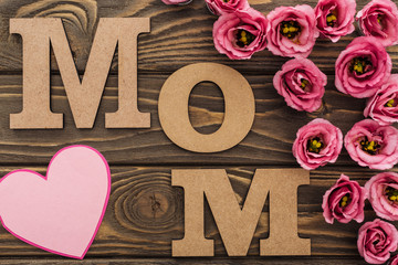 top view of pink eustoma flowers, paper heart and mom word on wooden table