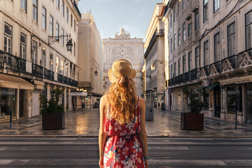 Fototapeta premium Woman in red dress and hat walking through Lisbon city centre