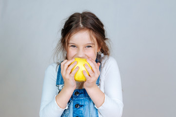 Emotional portrait little beautiful girl with pigtails in jeans overalls eating bites holding an...