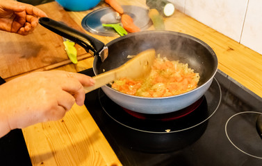 a person stirring a sauce in a pan carrying carrots, onions, peppers and courgettes
