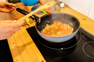 a person stirring a sauce in a pan carrying carrots, onions, peppers and courgettes