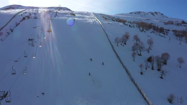 Aerial, reverse, drone shot away from people skiing down hill, on the slopes of Leitariegos ski resort, on a sunny day, in Leon, Spain