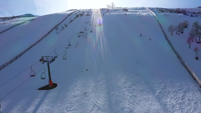Aerial, drone shot towards lifts and people skiing down hill, on the slopes of Leitariegos ski resort, on a sunny day, in Leon, Spain