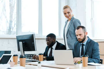 attractive business coach near multicultural coworkers in office