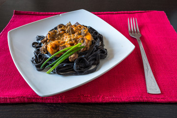 black pasta with cuttlefish ink. Pasta of durum wheat semolina with squid ink with beef and sweet pepper sauce on a square plate decorated with green onions with fork