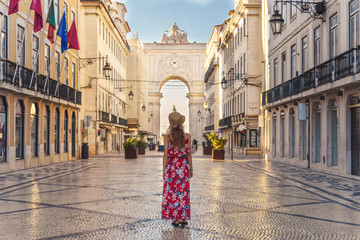 Woman in red dress walking through Praca Do Comercio and looking at Arco da Rua Augusta with...