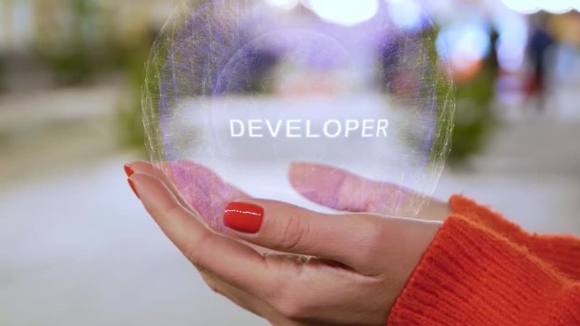Female hands holding a conceptual hologram with text Developer. Woman with red nails and sweater with future holographic technology on a blurred background of the street
