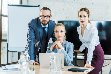 attractive businesswomen near bearded businessman and laptop in conference room