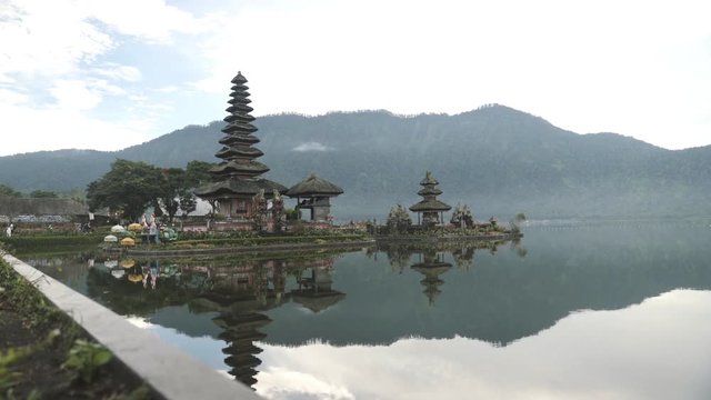 Pura Ulun Danu Beratan shaivite temple and mountains reflected in Bratan lake on overcast day in Bali, Indonesia. Steady long shot.