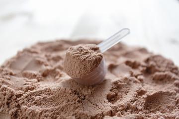 Product photograph of spoon or measuring scoop of whey protein. Whey protein powder sports bodybuilding supplement. Plastic scoop on wooden background with chocolate powder flavour.