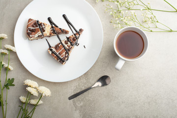 On the plate are two slices of cheesecake with tea and flowers, with space for congratulations
