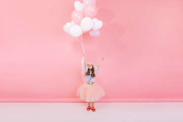 Happy brightful image of excited joyful little girl in tulle skirt holding ribbon with flying...